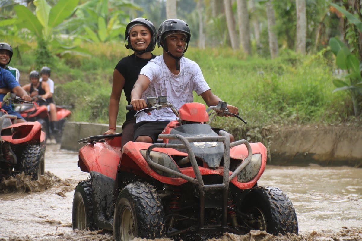 Two riders crossing a muddy river on an ATV