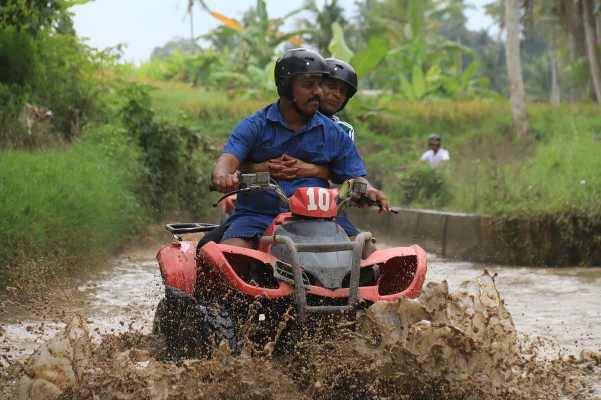 ATV splashing mud with green rice fields behind