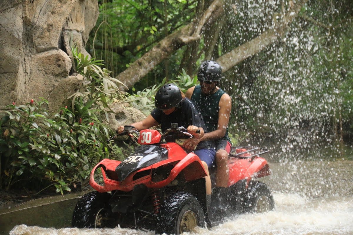 Riders passing under a waterfall beside a rock face