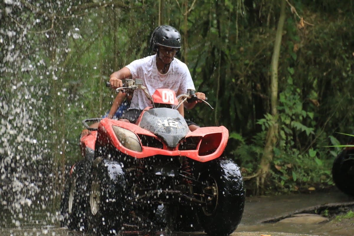 Rider bursting through a waterfall spray on an ATV