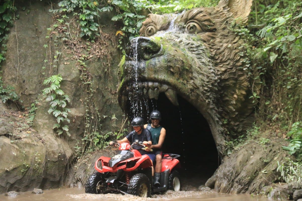 Two riders on an ATV at the carved beast-head cave waterfall