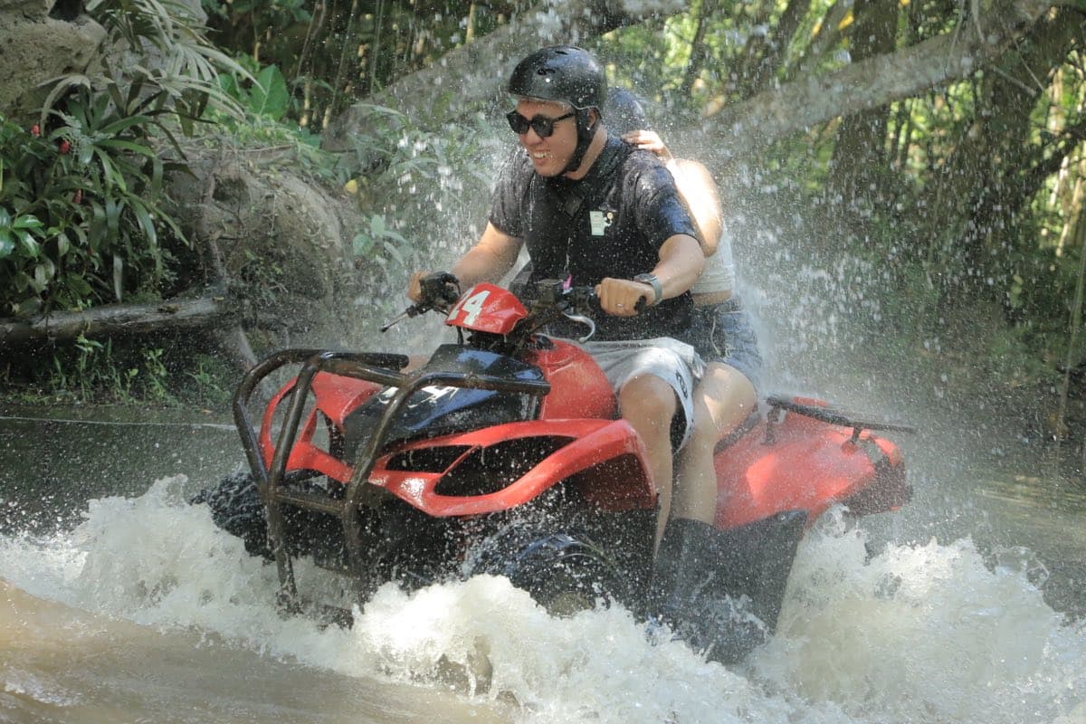 Rider powering an ATV through a sunlit river