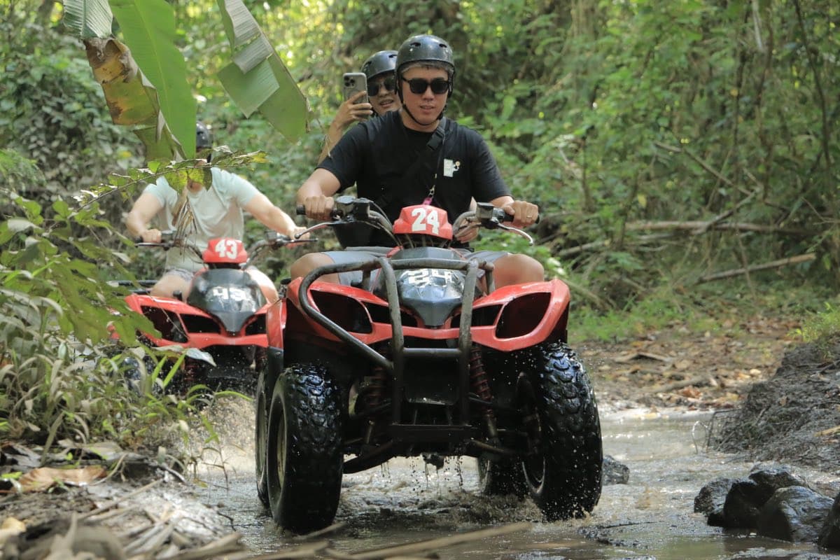 Riders following a muddy jungle trail on ATVs
